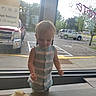 child, toddler, standing, indoors, window, restaurant, cafe, pastry, food, table, striped_outfit, blond_hair, face, person, parking_lot, vehicles, storefront, daylight, candid, portrait