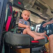 Vance is registered to the contest to win money with this photo: child, toddler, baby, fire_engine, vehicle, seat, safety_harness, rescue_equipment, firefighter_gear, interior, helmet, control_panel, adult, tattoo, barefoot, blond_hair, portrait, sitting, indoor, emergency_vehicle