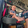 child, toddler, baby, fire_engine, vehicle, seat, safety_harness, rescue_equipment, firefighter_gear, interior, helmet, control_panel, adult, tattoo, barefoot, blond_hair, portrait, sitting, indoor, emergency_vehicle