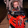 baby, child, sleeping, stroller, blanket, nighttime, outdoor, portrait, infant, seated, harness, carriage, orange_blanket, patterned_blanket, sidewalk, driveway, residential_area, streetlight, flash_photography, tired