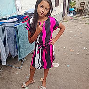 Naissy participe au concours pour gagner de l'argent avec cette photo : child, girl, dress, peace_sign, outdoor, laundry, drying_rack, smiley_face, concrete, footwear, hand_on_hip, long_hair, patterned_clothing, wall, window, door, chair, plant, casual, portrait