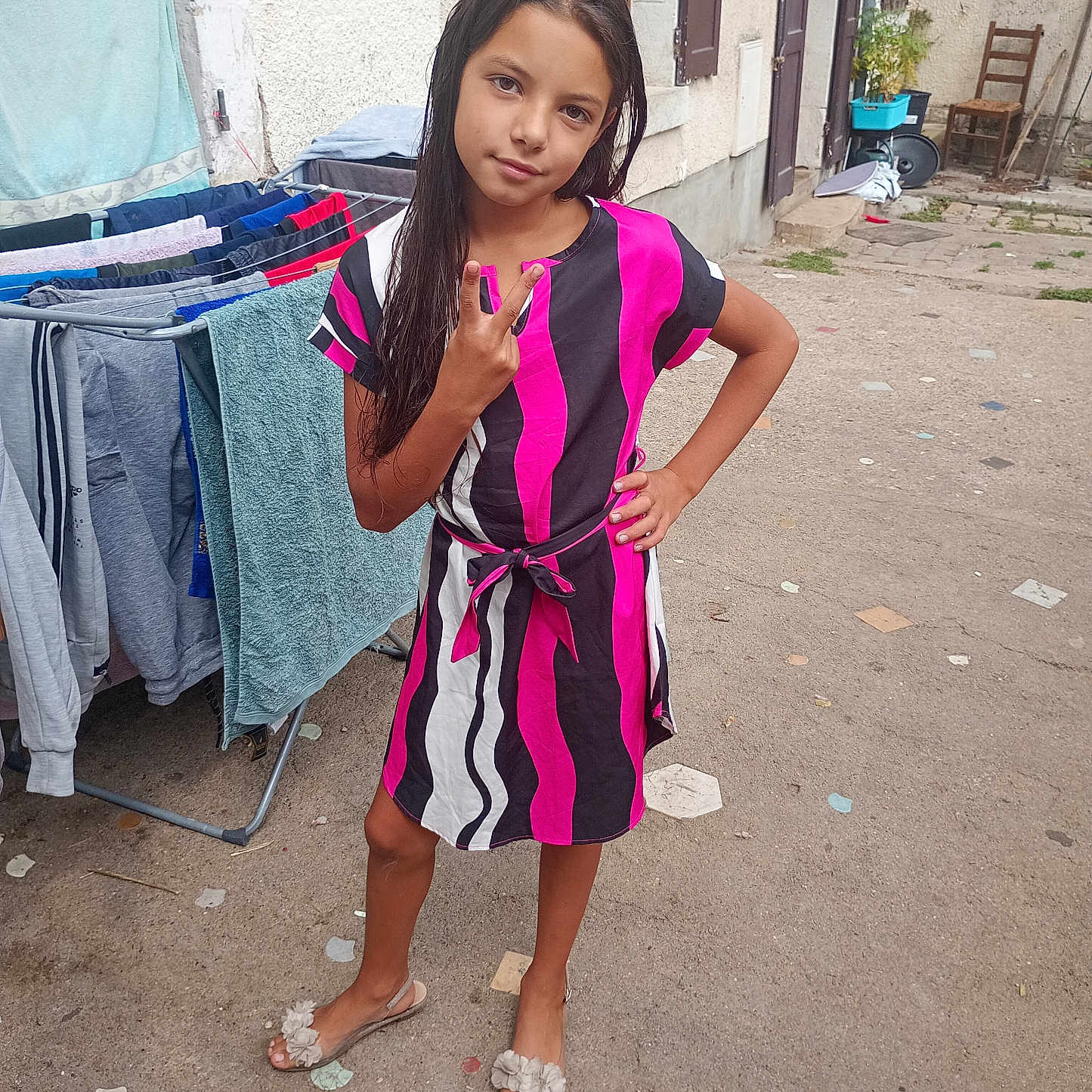 Naissy participe au concours pour gagner de l'argent avec cette photo : casual, chair, child, concrete, door, dress, drying_rack, footwear, girl, hand_on_hip, laundry, long_hair, outdoor, patterned_clothing, peace_sign, plant, portrait, smiley_face, wall, window