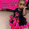 toddler, child, girl, black_hair, pink_bow, black_dress, pink_ribbons, floor, indoor, portrait, expression, attitude, cartoon, table, letters, celebration, party, colorful, cute, fashion