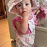 toddler, child, baby, hat, romper, flower_pattern, mirror, reflection, indoor, floor_tiles, curious, blue_eyes, pink_clothing, standing, finger_in_mouth, home, blanket, doorway, wooden_furniture, soft_lighting
