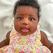 Jade participe au concours pour gagner de l'argent avec cette photo : baby, child, infant, face, eyes, mouth, curly_hair, flower_dress, colorful, cute, portrait, skin, person, sitting, closeup, soft_background, innocence, young, happy, smiling