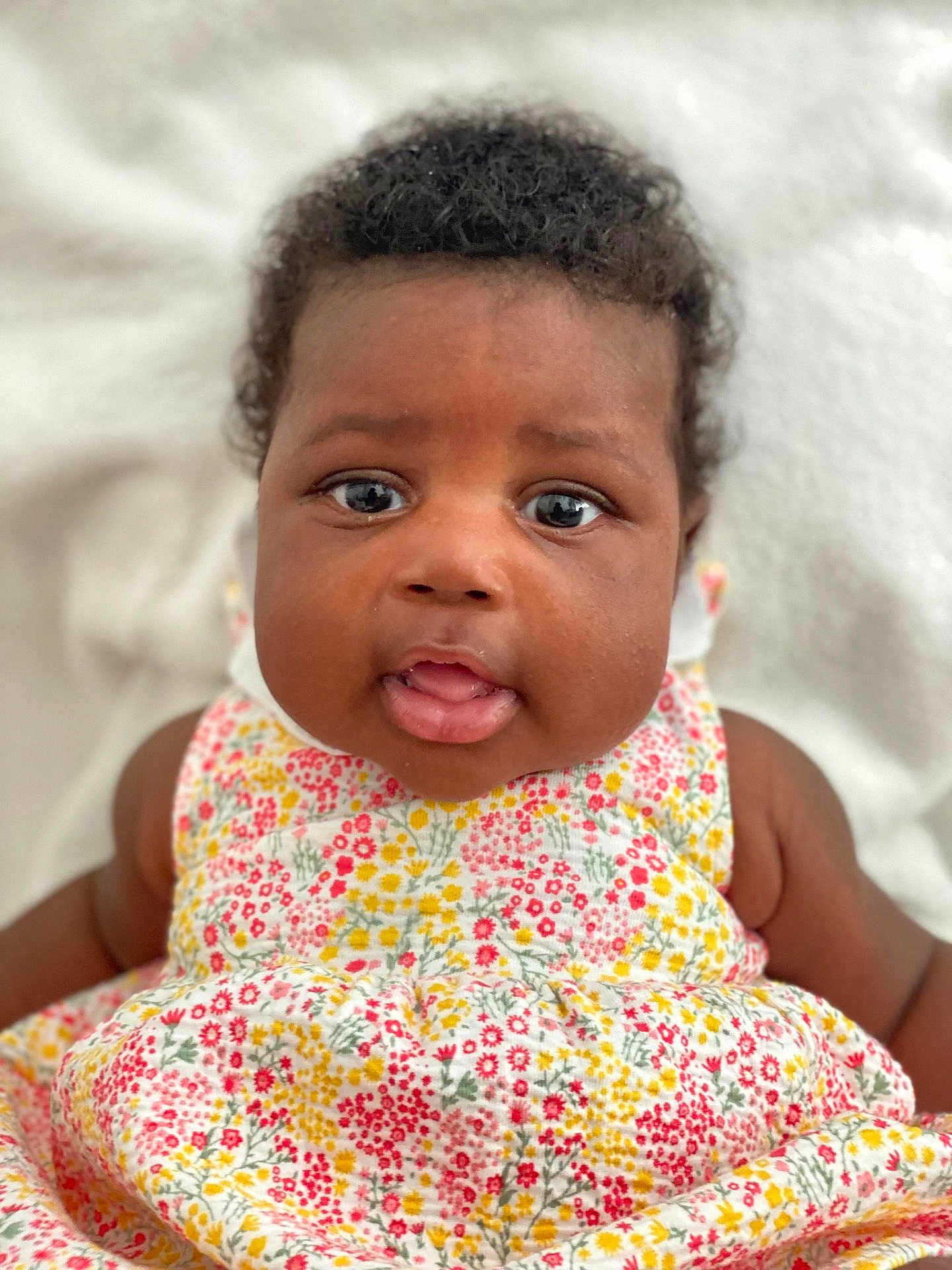 Jade participe au concours pour gagner de l'argent avec cette photo : baby, child, infant, face, eyes, mouth, curly_hair, flower_dress, colorful, cute, portrait, skin, person, sitting, closeup, soft_background, innocence, young, happy, smiling