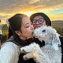 affection, casual_clothing, clouds, couple, dog, fur, glasses, grass, happy, hat, holding, kiss, love, man, nature, outdoor, portrait, sky, sunset, woman