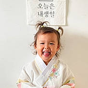 Yuna participe au concours pour gagner de l'argent avec cette photo : child, toddler, hanbok, traditional_clothing, smiling, pigtails, birthday, banner, cake_illustration, wall, indoors, happy, cute, portrait, celebration, colorful, flower_embroidery, young_child, person, asian_child