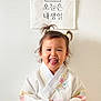 child, toddler, hanbok, traditional_clothing, smiling, pigtails, birthday, banner, cake_illustration, wall, indoors, happy, cute, portrait, celebration, colorful, flower_embroidery, young_child, person, asian_child
