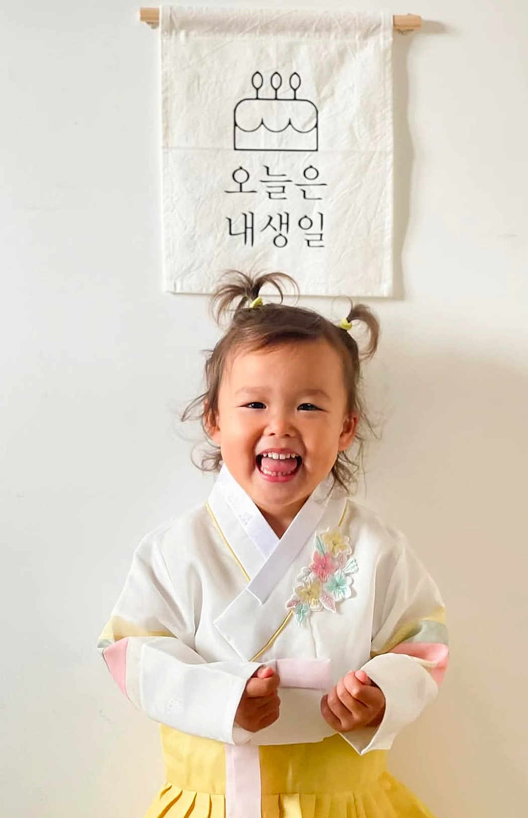 Yuna participe au concours pour gagner de l'argent avec cette photo : child, toddler, hanbok, traditional_clothing, smiling, pigtails, birthday, banner, cake_illustration, wall, indoors, happy, cute, portrait, celebration, colorful, flower_embroidery, young_child, person, asian_child