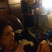Diamond is registered to the contest to win money with this photo: woman, cat, indoor, dim_lighting, table, cups, snacks, refrigerator, chair, clutter, intimate, holding, black_and_white_cat, casual, relaxed, home, person, furniture, evening, cozy