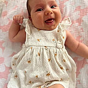 Alice participe au concours pour gagner de l'argent avec cette photo : baby, smiling, infant, dress, white_clothing, floral_pattern, blanket, pink, lying_down, tongue_out, cute, happy, child, skin, face, arm, leg, person, indoors, closeup