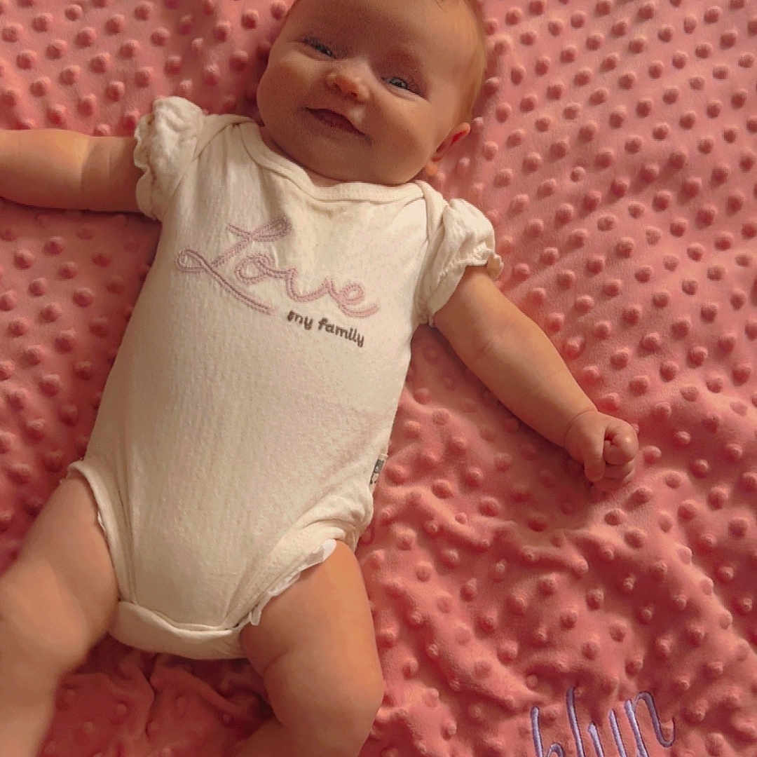 Brooklyn joined the competition — help win amazing prizes! baby, bed, blanket, child, close_up, clothing, embroidered, face, family, happy, indoor, infant, lying_down, name, onesie, pink, plush, portrait, relaxed, smiling