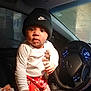 toddler, child, baby, car_interior, steering_wheel, rainy_window, nike_beanie, mickey_mouse_pants, hand, clothing, seat, dashboard, lights, person, indoor, portrait, cute, expression, night, support