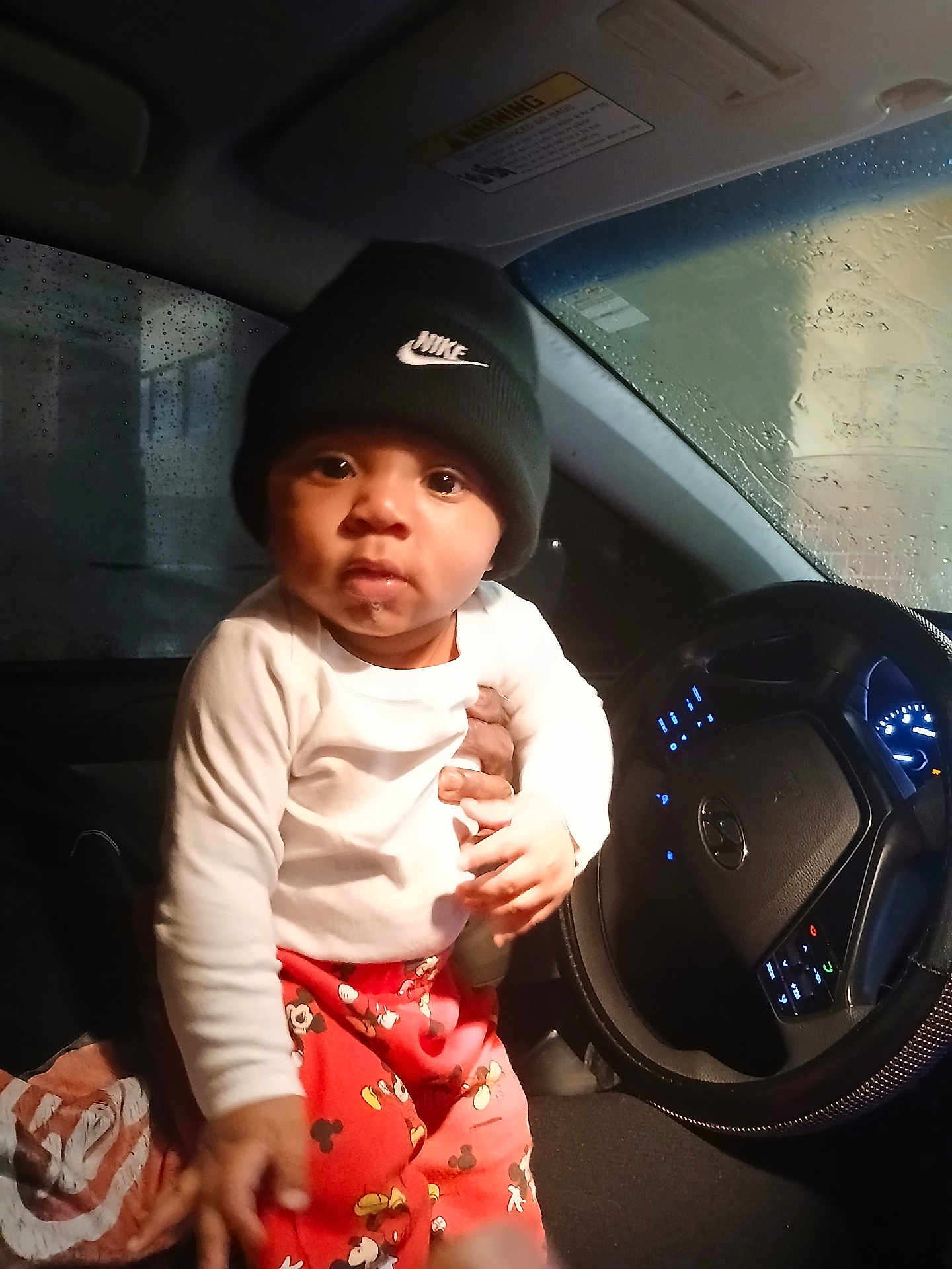 Zymir joined the competition — help win amazing prizes! toddler, child, baby, car_interior, steering_wheel, rainy_window, nike_beanie, mickey_mouse_pants, hand, clothing, seat, dashboard, lights, person, indoor, portrait, cute, expression, night, support
