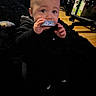 Elliott is registered to the contest to win money with this photo: baby, child, infant, portrait, indoors, sitting, curious, snack, wrapper, hands, face, eyes, smiling, black_clothing, hoodie, rug, stroller, wood_floor, home, photography