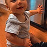 baby, child, smiling, sitting, indoor, portrait, wooden_floor, gray_clothing, short_sleeves, socks, appliance, home, happy, gummy_smile, reaching, hands, kneeling, warm_lighting, face, photography