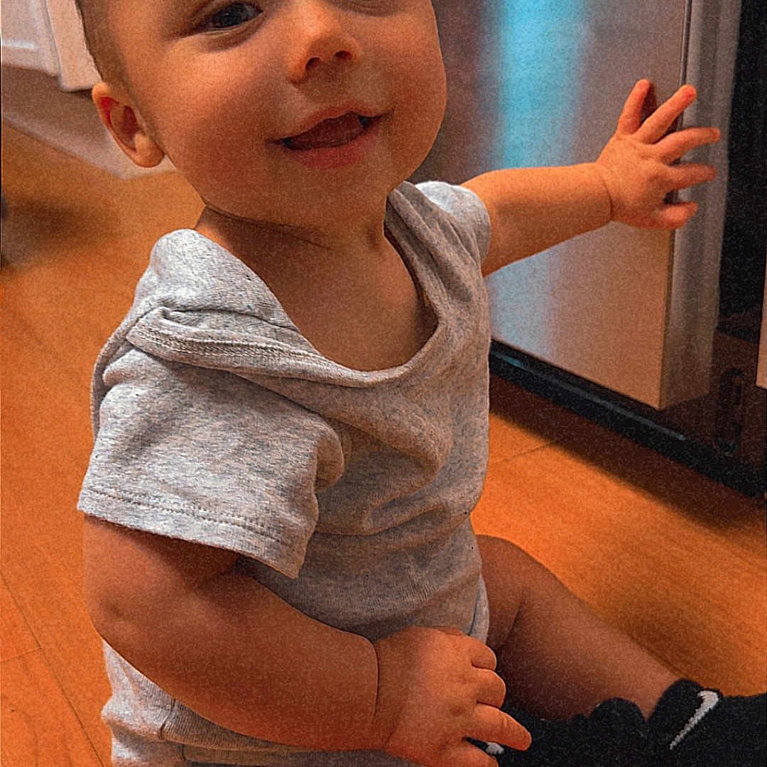 Elliott is registered to the contest to win money with this photo: baby, child, smiling, sitting, indoor, portrait, wooden_floor, gray_clothing, short_sleeves, socks, appliance, home, happy, gummy_smile, reaching, hands, kneeling, warm_lighting, face, photography