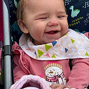 Amaya is registered to the contest to win money with this photo: baby, smiling, stroller, bib, pink_clothing, blanket, snowman_print, child, happy, cute, infant, outdoor, dinosaur_pattern, seat, person, portrait, warm_clothing, hands, face, head