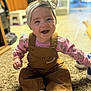 Amaya is registered to the contest to win money with this photo: baby, child, smiling, headband, overalls, sitting, carpet, indoor, happy, cute, clothing, footwear, infant, portrait, person, toddler, pink, brown, white_socks, home