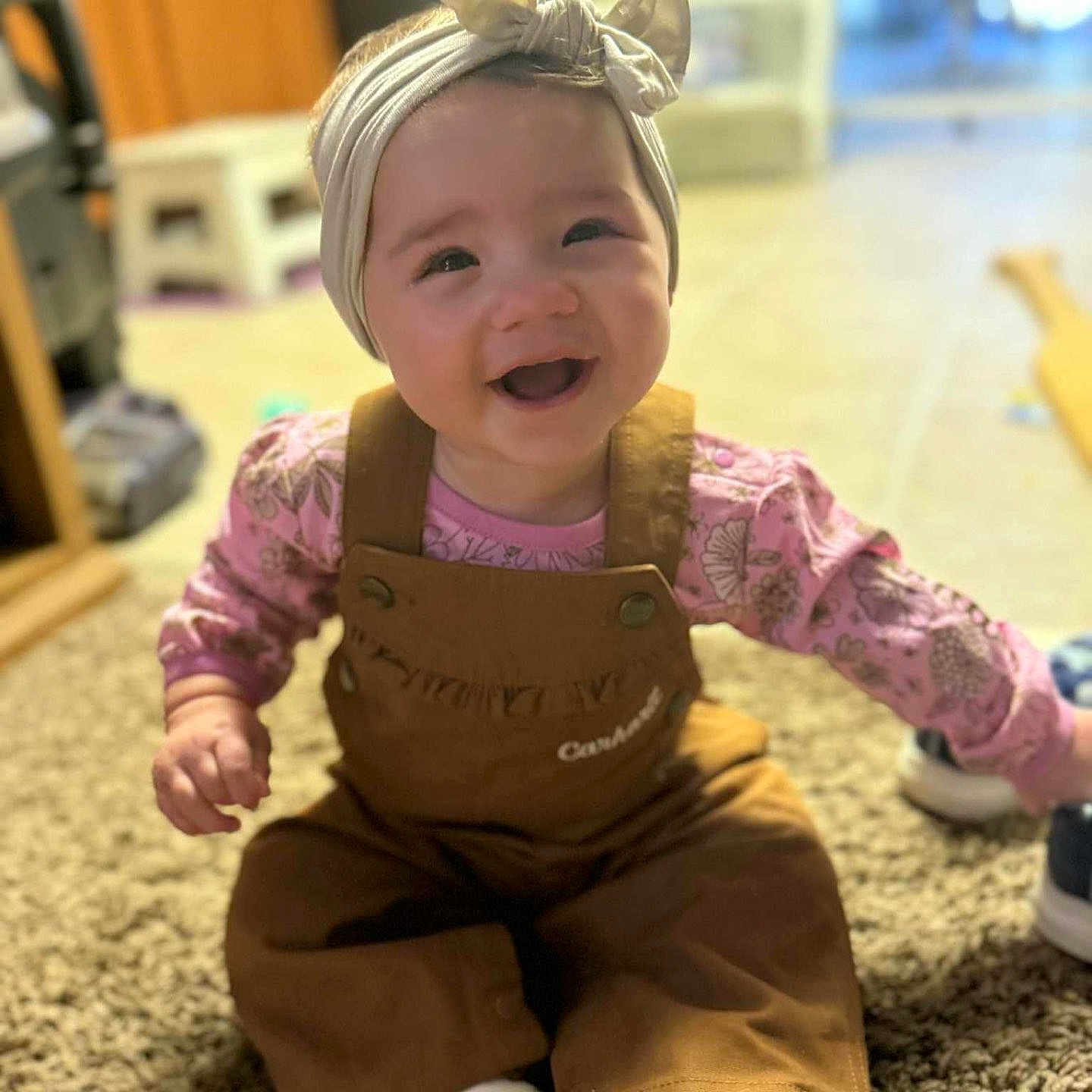 Amaya is registered to the contest to win money with this photo: baby, brown, carpet, child, clothing, cute, footwear, happy, headband, home, indoor, infant, overalls, person, pink, portrait, sitting, smiling, toddler, white_socks