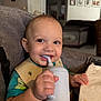 Kairo is registered to the contest to win money with this photo: baby, child, smiling, high_chair, sippy_cup, bib, indoor, happy, portrait, person, hand, table, clothing, face, drinking, young_child, cute, home, seat, expression