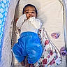 baby, baby_clothes, blanket, blue_pants, child, cozy, crib, cute, face, floral_pattern, indoor, infant, newborn, nursery, portrait, resting, sleeping_area, socks, soft_lighting, white_shirt