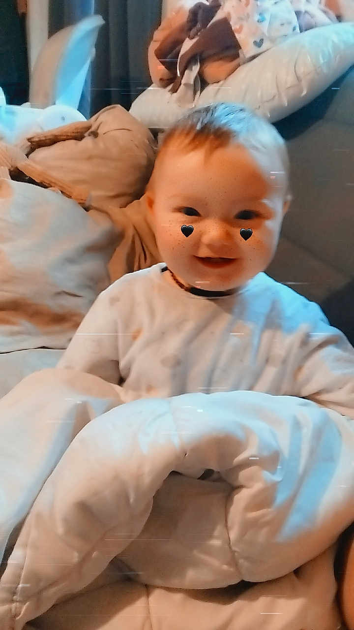 Jade participe au concours pour gagner de l'argent avec cette photo : baby, smile, blanket, pillow, indoor, child, cute, face, freckles, heart_stickers, cozy, soft_lighting, happy, infant, clothing, portrait, home, warm, comfort, sitting