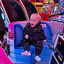 Arlo is registered to the contest to win money with this photo: toddler, child, amusement_ride, arcade, neon_lights, seat_belt, joyful, indoor, playful, colorful, entertainment, arcade_machine, casual_clothing, nike_logo, footwear, smiling, fun, game_center, young_child, seat