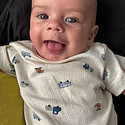 Kailum is registered to the contest to win money with this photo: baby, smiling, tongue_out, onesie, vehicle_print, infant, happy, cute, child, face, head, clothing, cushion, black_background, green_cushion, portrait, closeup, skin, eyes, mouth