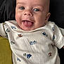 baby, smiling, tongue_out, onesie, vehicle_print, infant, happy, cute, child, face, head, clothing, cushion, black_background, green_cushion, portrait, closeup, skin, eyes, mouth