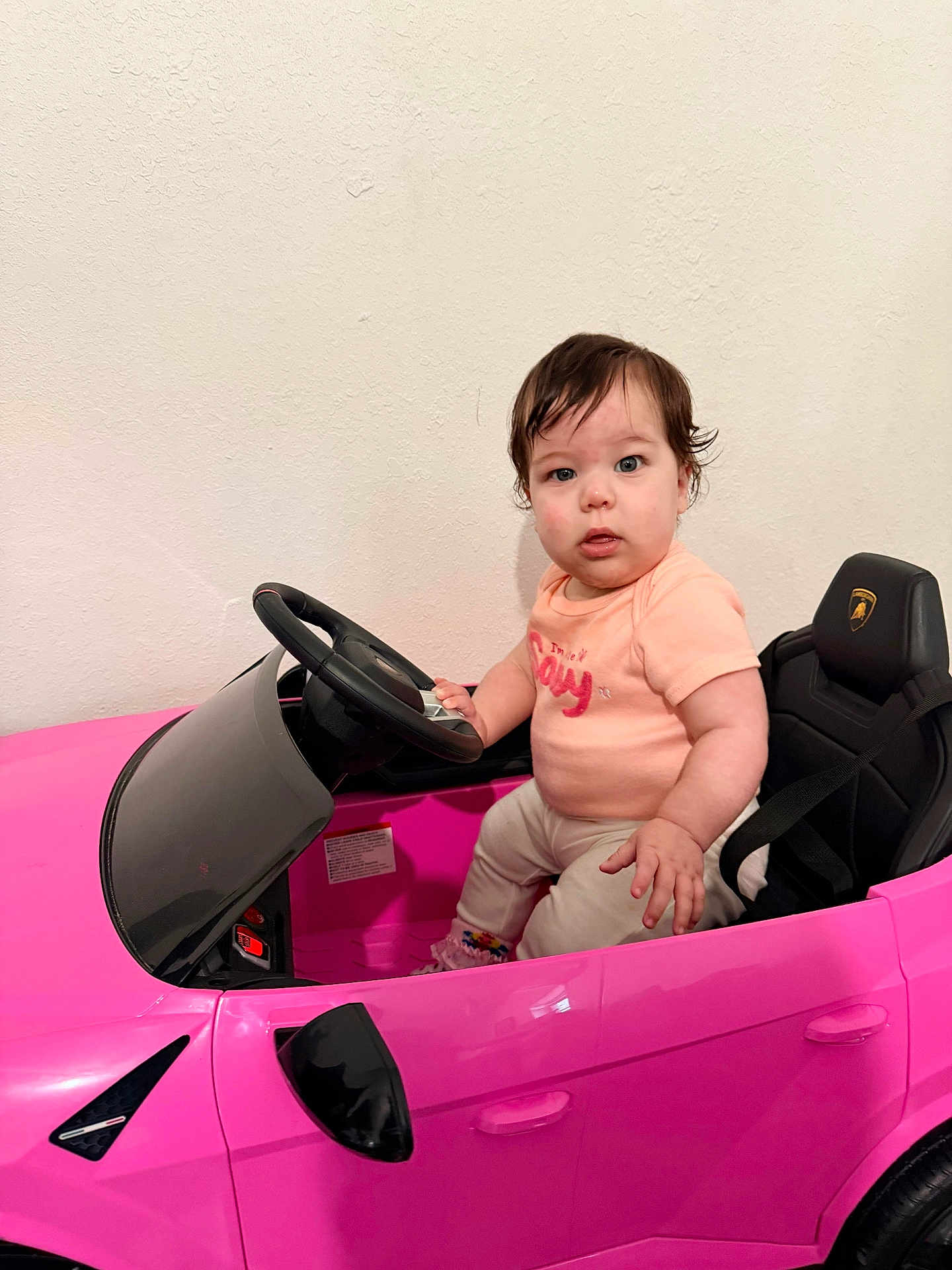 Valerie joined the competition — help win amazing prizes! toddler, child, toy_car, pink, steering_wheel, indoor, wall, seat, clothing, person, young_child, play, vehicle, serious, sitting, hair, face, eyes, hands, footwear