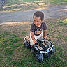 child, toy_vehicle, grass, tree, fence, parked_car, outdoor, daylight, clothing, shoes, expression, play, vehicle, nature, sidewalk, park, person, young_child, casual, sunlight