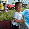 child, pool, water, wet, bracelet, white_shirt, black_shorts, outdoor, grass, party, table, chair, tent, toy, person, daytime, backyard, curly_hair, expression, summer