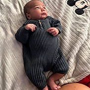 Javier is registered to the contest to win money with this photo: baby, infant, blanket, mickey_mouse, onesie, clothing, feet, hands, face, person, soft_texture, lying_down, looking_up, indoor, cute, newborn, skin, warm_colors, cozy, child