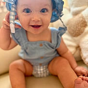 Emelia is registered to the contest to win money with this photo: baby, child, smiling, blue_hat, blue_clothing, sitting, indoor, couch, happy, cute, infant, portrait, feet, face, person, young_child, plaid, button, skin, headwear