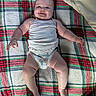 baby, infant, child, smiling, lying_down, portrait, face, eyes, arms, legs, diaper, onesie, blanket, plaid, bedding, pillow, toy, indoor, happy, cozy