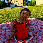 Amira joined the competition — help win amazing prizes! baby, child, smiling, curly_hair, hair_clip, watermelon_cake, berries, picnic_blanket, cherry_pattern, outdoor, grass, sunlight, plate, happy, sitting, summer, food, fruit, nature, portrait