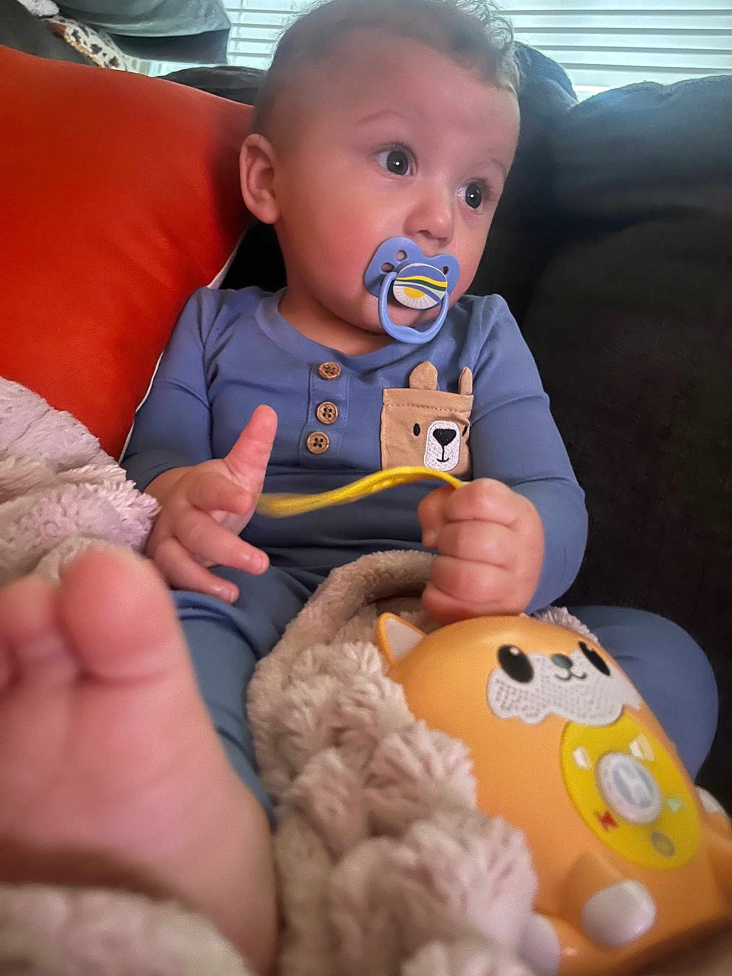 Hudson is registered to the contest to win money with this photo: baby, pacifier, toy, blanket, pajamas, couch, orange_cushion, child, foot, hand, face, indoor, plush, comfort, cute, infant, relaxing, portrait, young_child, blue_clothing