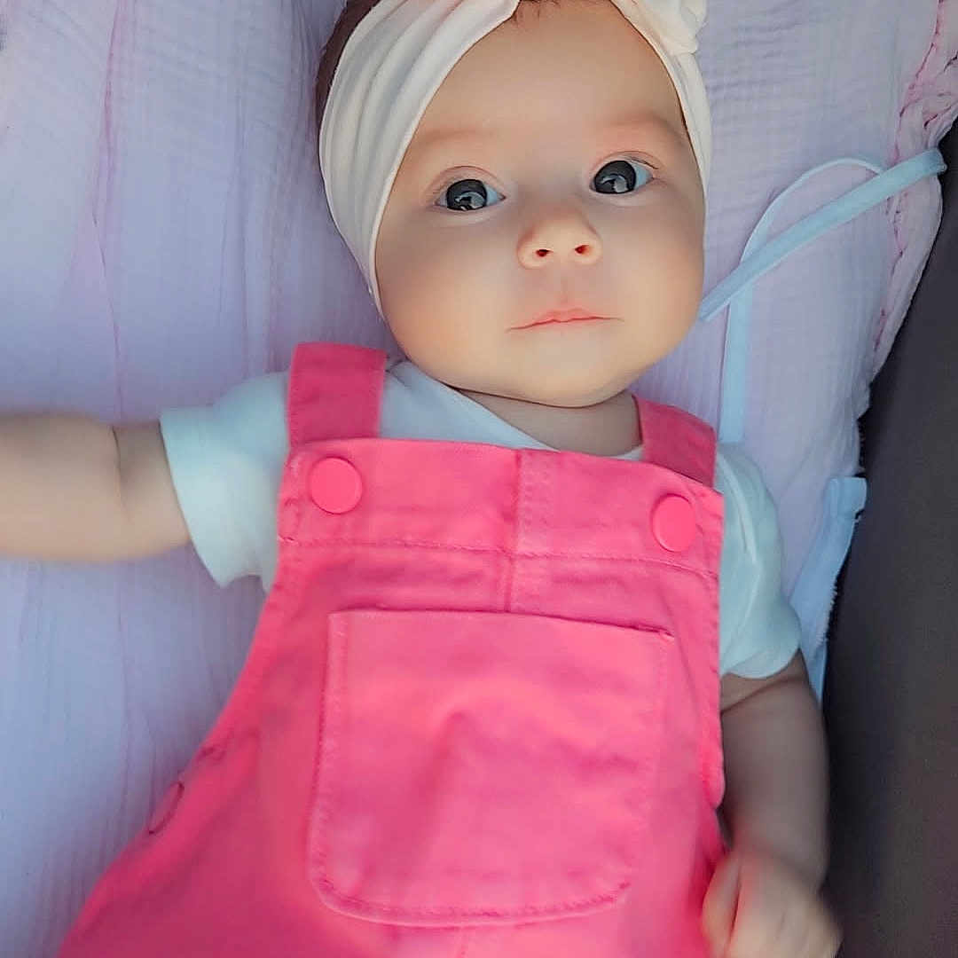 Romy a rejoint le concours — aidez-le/la à gagner de superbes lots ! baby, baby_fashion, blanket, child, closeup, clothing, cute, face, headband, headwear, indoors, infant, infant_girl, lying_down, peaceful, pink_overall, portrait, skin, small_hand, soft_texture