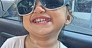Azeneth is registered to the contest to win money with this photo: braces, brown_hair, car, car_interior, child, close_up, floral_design, happy, long_hair, outdoor, pink_shirt, playful, portrait, seated, smiling, storefront, sunglasses, sunlight, teeth, window