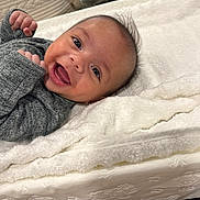 Everett is registered to the contest to win money with this photo: baby, smiling, infant, blanket, gray_clothing, face, happy, lying_down, fist, cute, indoors, soft_texture, young_child, portrait, head, skin, expression, person, warm, cozy