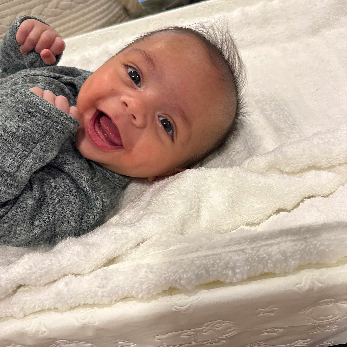 Everett is registered to the contest to win money with this photo: baby, blanket, cozy, cute, expression, face, fist, gray_clothing, happy, head, indoors, infant, lying_down, person, portrait, skin, smiling, soft_texture, warm, young_child