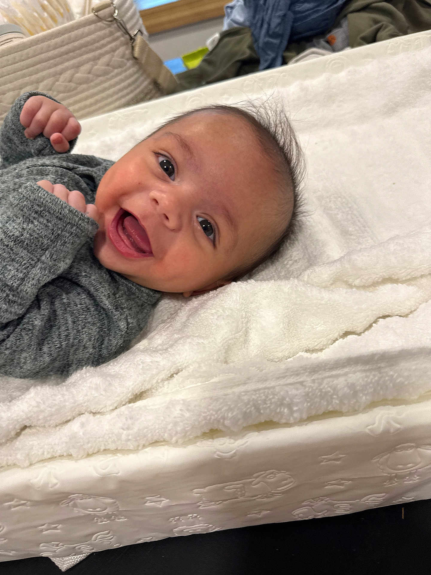 Everett is registered to the contest to win money with this photo: baby, smiling, infant, blanket, gray_clothing, face, happy, lying_down, fist, cute, indoors, soft_texture, young_child, portrait, head, skin, expression, person, warm, cozy