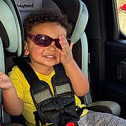Jason is registered to the contest to win money with this photo: toddler, child, car_seat, sunglasses, yellow_shirt, seatbelt, car_interior, smiling, curly_hair, hand, window, clothing, babytrend, safety_harness, playful, seat, child_safety, casual, fun, portrait