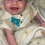George-David is registered to the contest to win money with this photo: baby, smiling, pacifier, blanket, clothing, infant, cute, happy, face, skin, hand, sitting, closeup, indoors, soft_texture, comfort, child, portrait, young, baby_girl