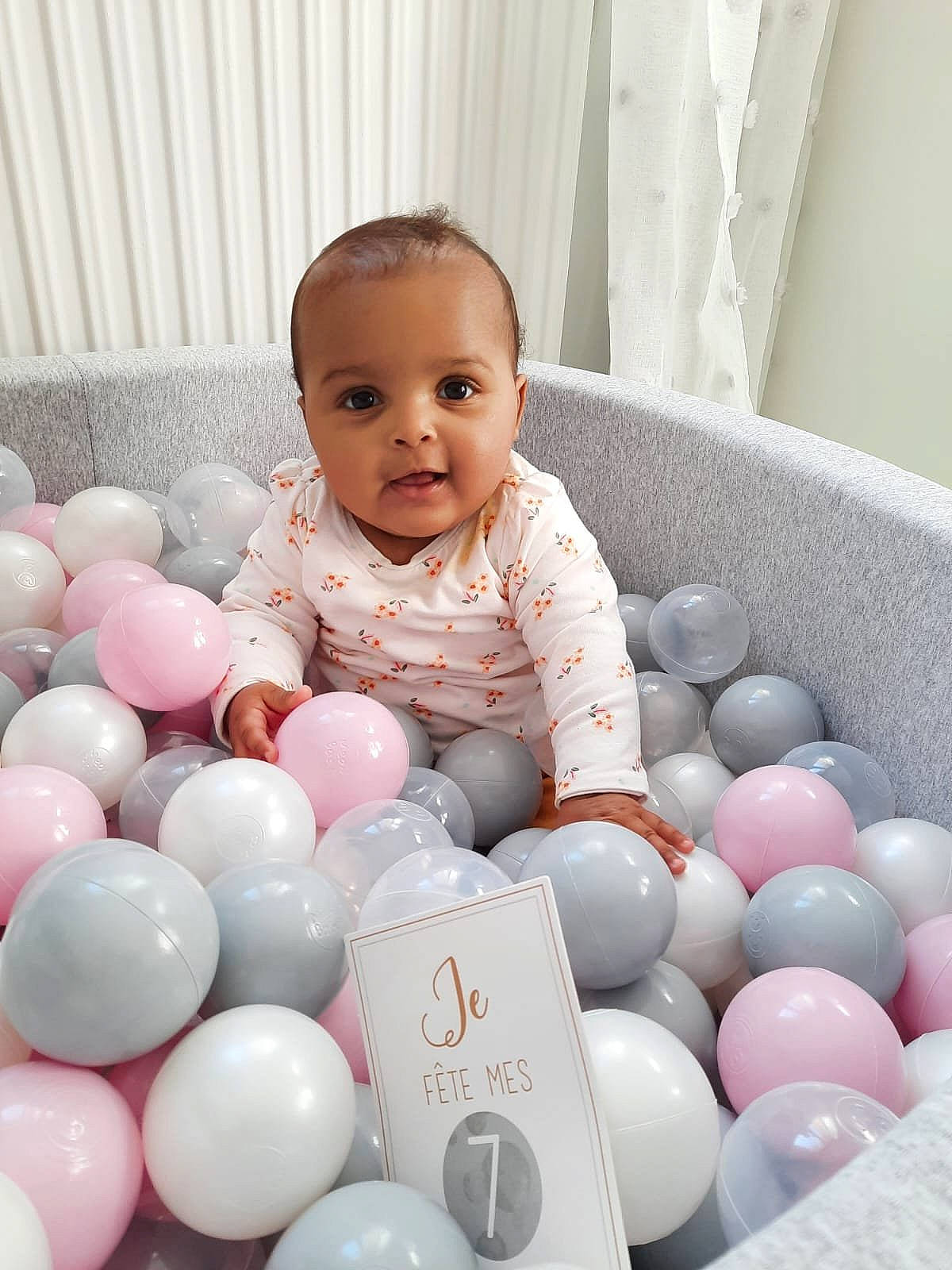 Mariana participe au concours pour gagner de l'argent avec cette photo : baby, baby_toddler_clothing, balloon, beauty, child, comfort, event, eye, facial_expression, fun, happy, party_supply, people, person, product, room, sitting, skin, smile, toddler