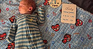Tiberius is registered to the contest to win money with this photo: baby, bed, blanket, cozy, face, family_photo, head, indoor, infant, lying_down, milestone_card, newborn, nursery, one_month, onesie, photography, portrait, race_car, sleeping, striped_clothing