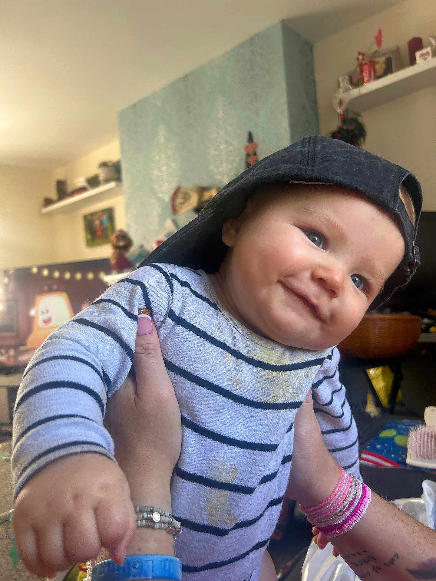 Teddy joined the competition — help win amazing prizes! baby, child, smiling, striped_shirt, cap, backwards_cap, hand, bracelet, tattoo, indoor, room, furniture, decorations, person, portrait, happy, face, closeup, infant, playful