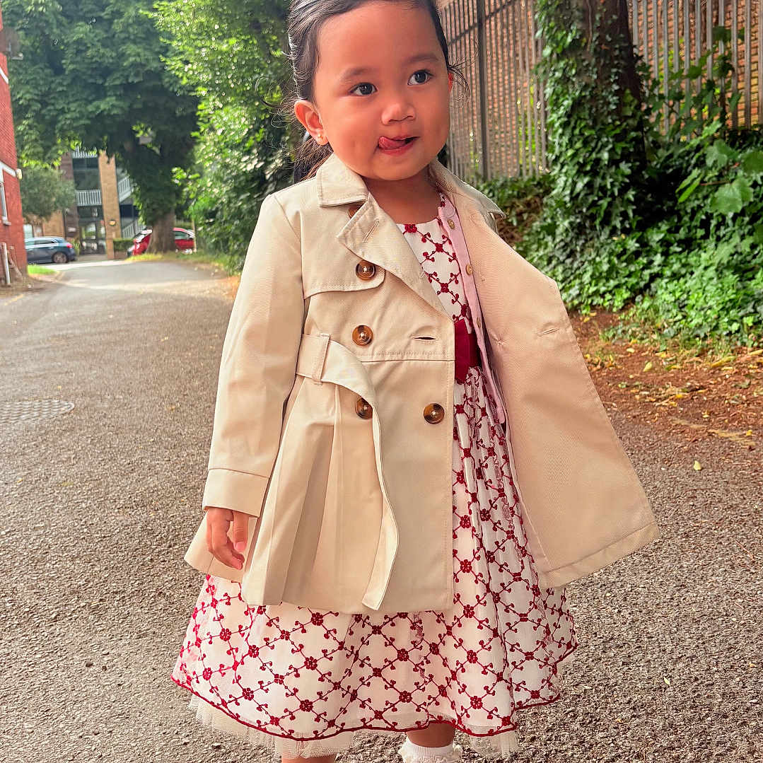 Zia joined the competition — help win amazing prizes! brick_wall, child, coat, daylight, dress, expression, fashion, footwear, girl, greenery, nature, outdoor, person, playful, sidewalk, smiling, socks, street, trees, young